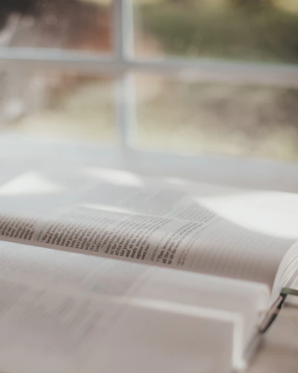 Sunlight softly shining through an open Bible on a wooden table, symbolizing clarity and spiritual growth.