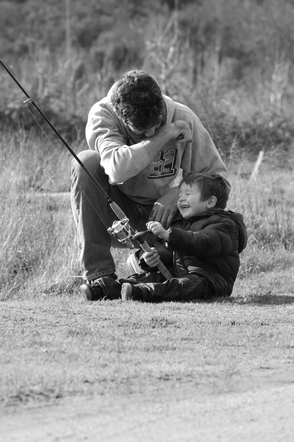 grayscale photo of man in hoodie playing with a baby