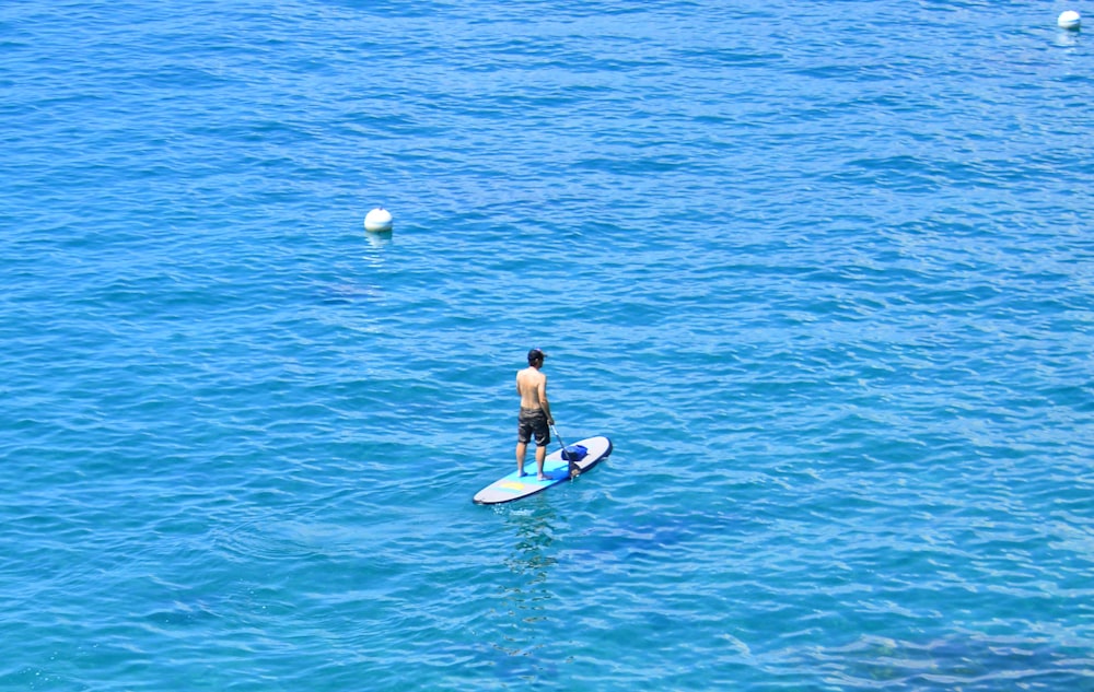 mulher no biquíni preto que monta na prancha de surf azul durante o dia