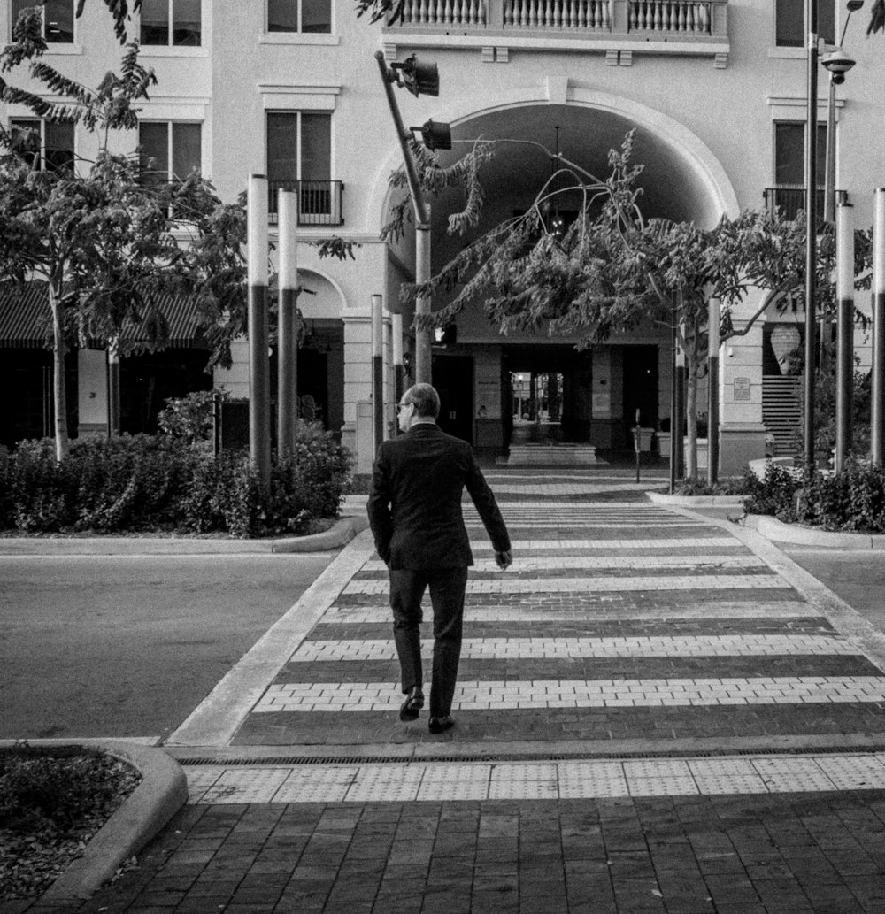 grayscale photo of man walking on pedestrian lane