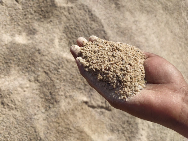 Hands holding a handful of mixed gravel and sand, highlighting texture and quality.