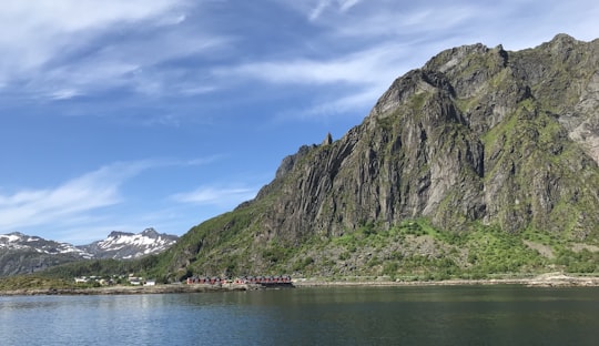 green and gray mountain beside body of water under blue sky during daytime in Lofoten Norway
