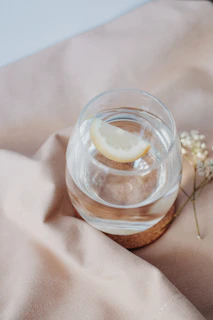 A glass of water with lemon slices placed on a bedside table next to a book.