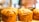 Golden brown, flaky loaves of bread displayed on a wooden surface with a blurred background, likely in a bakery setting.