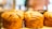 Golden brown, flaky loaves of bread displayed on a wooden surface with a blurred background, likely in a bakery setting.