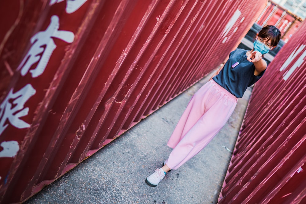 Mujer con hiyab azul y abaya blanca de pie junto a la pared de madera roja