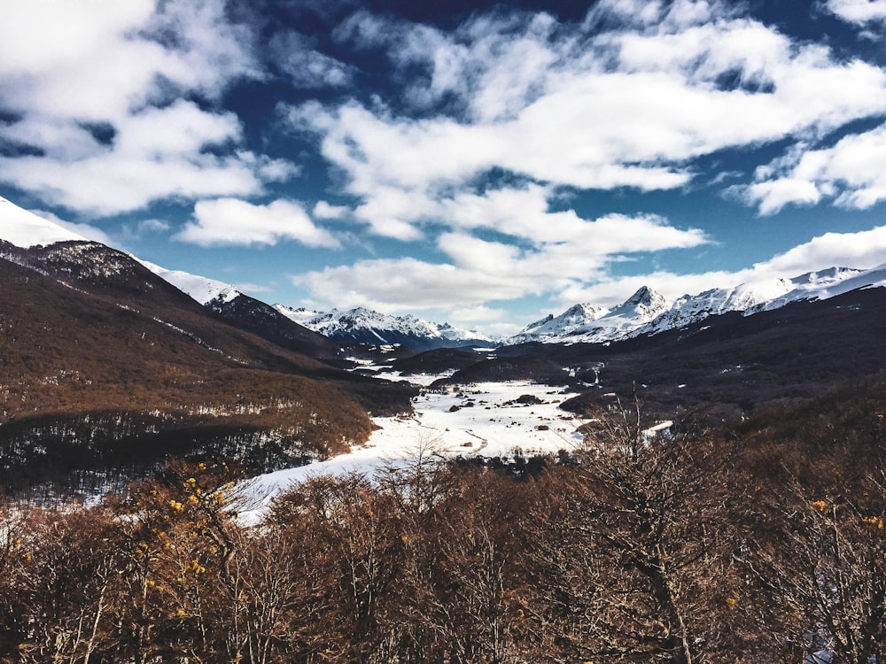 brown grass and snow covered mountains under white clouds and blue sky during daytime