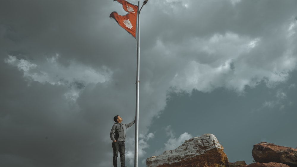 man in black jacket and black pants standing on rock under white clouds during daytime