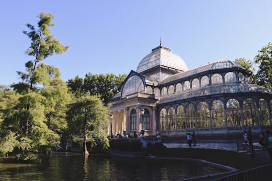 white and brown dome building near green trees and river during daytime in El Retiro Park Spain