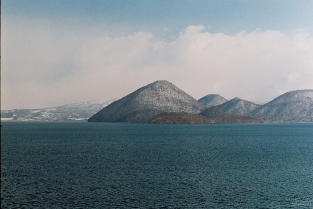 green mountain beside body of water under white clouds during daytime