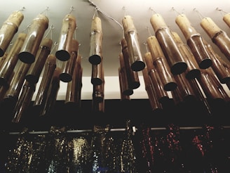 Hanging bamboo wind chimes arranged in a row, attached to the ceiling with metal hooks. Below them, there is a collection of shimmering, sequined fabrics in various colors.