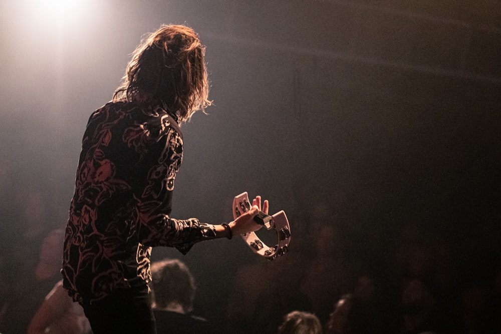 woman in black and red floral long sleeve shirt playing guitar on stage