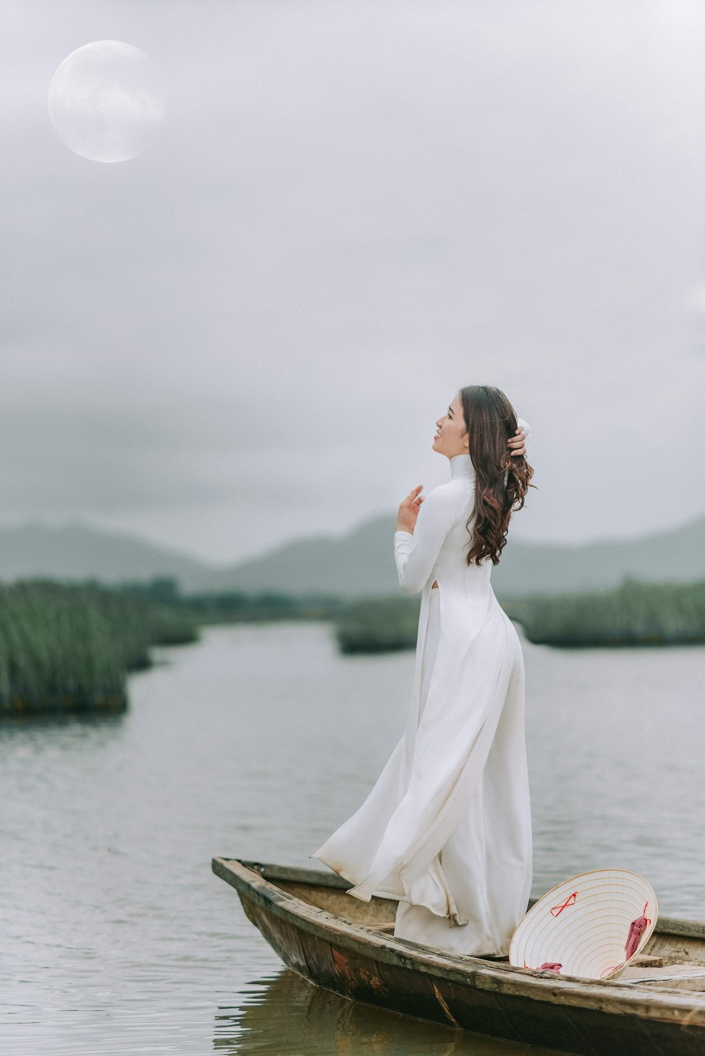 Mujer en vestido blanco de pie en un bote de madera marrón en el lago durante el día