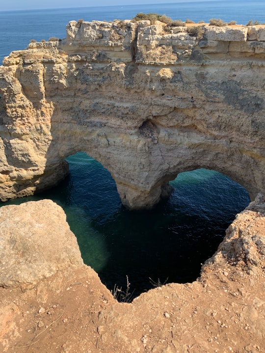 brown rock formation beside blue sea during daytime in Marinha beach Portugal