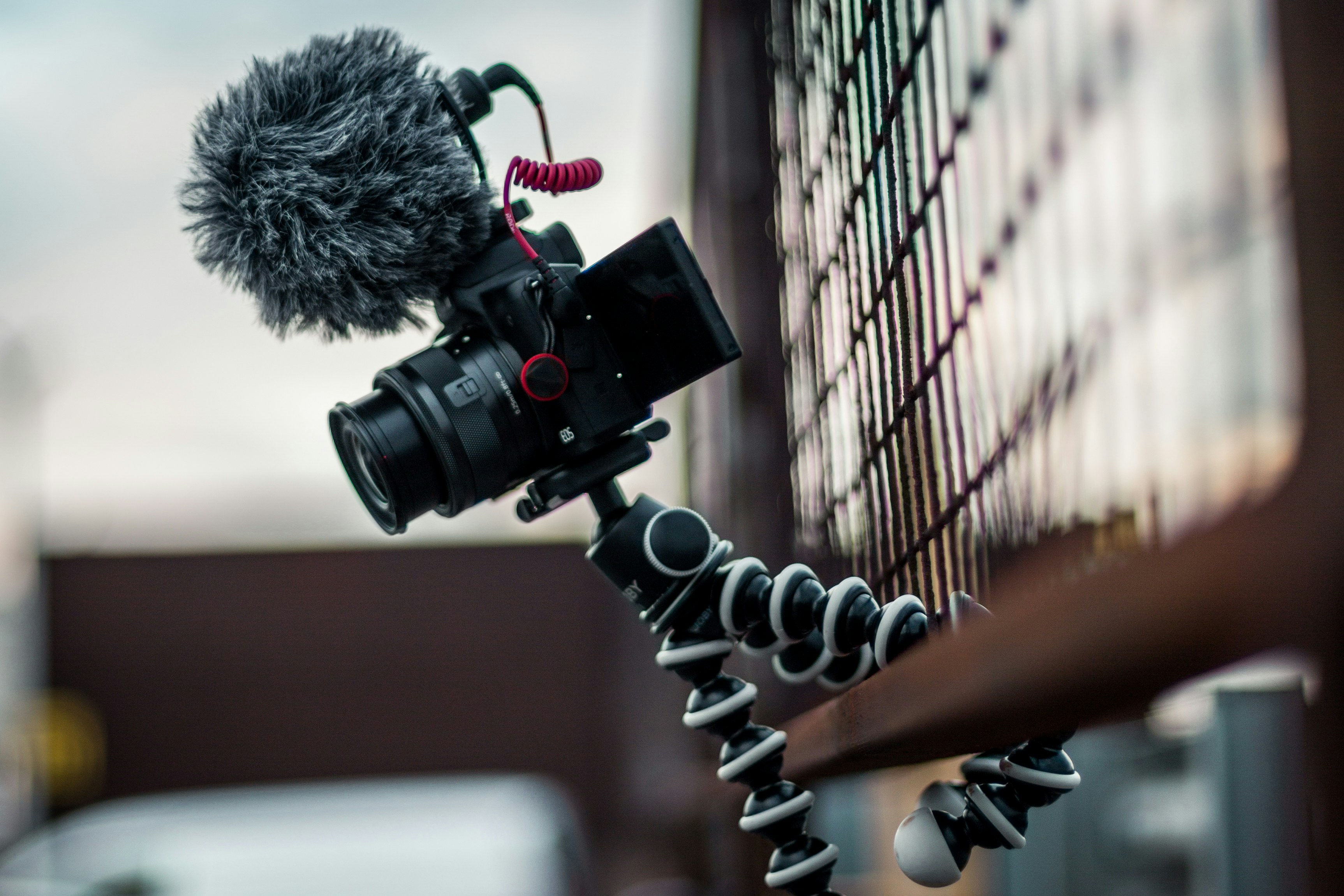 A DSLR camera stands on a tripod, with a microphone attached, capturing royalty free room tone sound for the video.