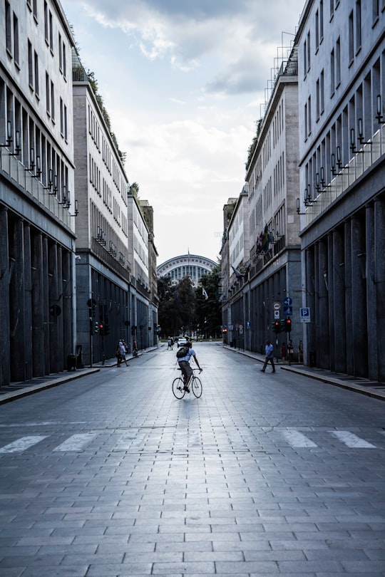 man in black jacket riding bicycle on road between high rise buildings during daytime in Milano Italy