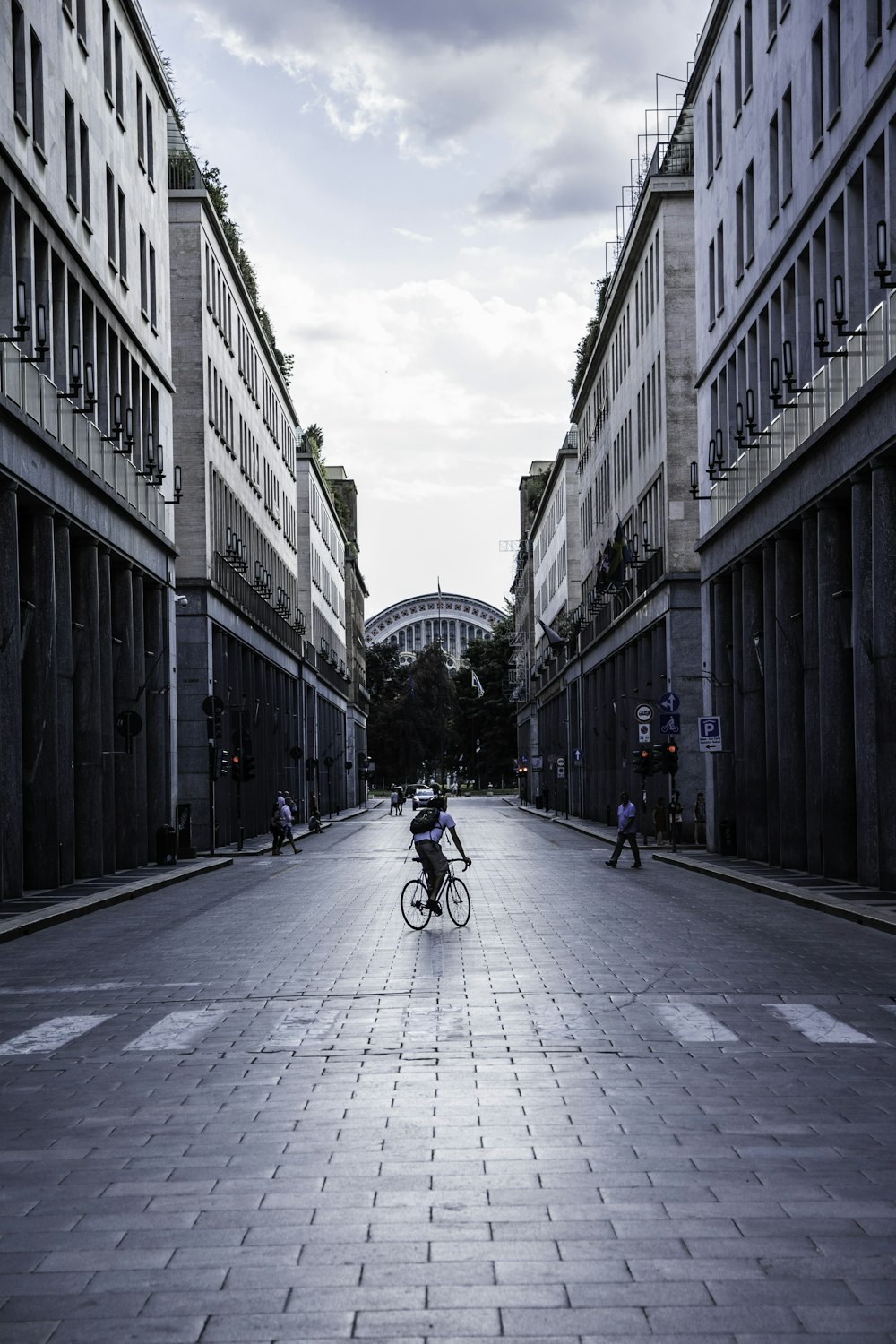 man in black jacket riding bicycle on road between high rise buildings during daytime