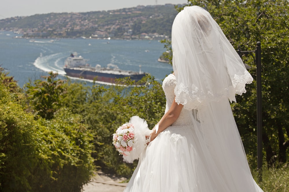 mujer en vestido de novia blanco sosteniendo ramo de flores
