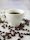 Man savoring a freshly brewed cup of coffee at a minimalist wooden table with coffee beans scattered nearby.