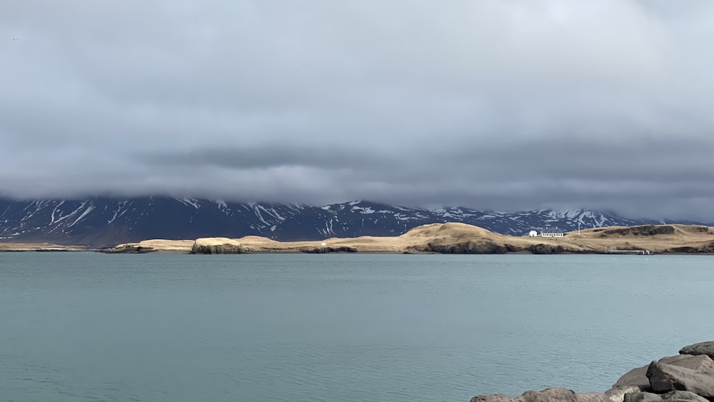 Montaña marrón cerca del cuerpo de agua bajo el cielo nublado durante el día