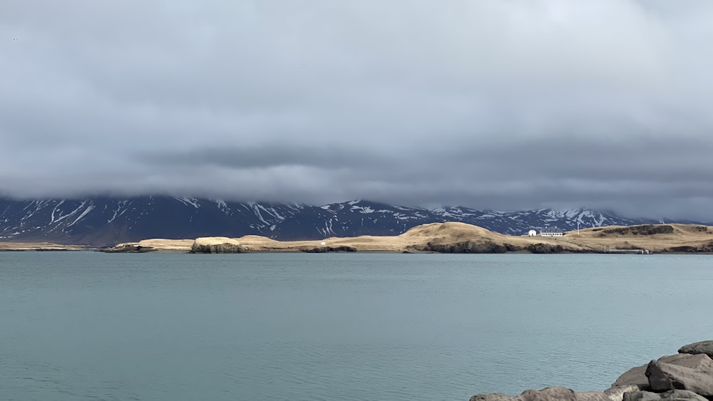 Montagna marrone vicino allo specchio d'acqua sotto il cielo nuvoloso durante il giorno