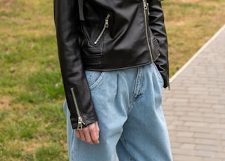 woman in black leather jacket and blue denim jeans standing on green grass field during daytime