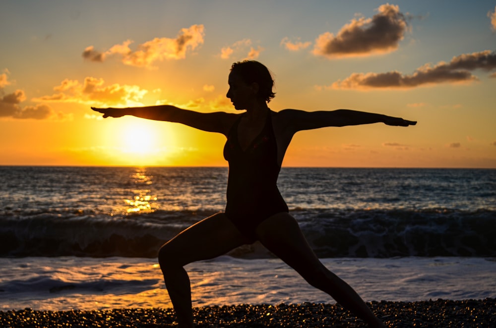 mulher no biquíni preto pulando na praia durante o pôr do sol