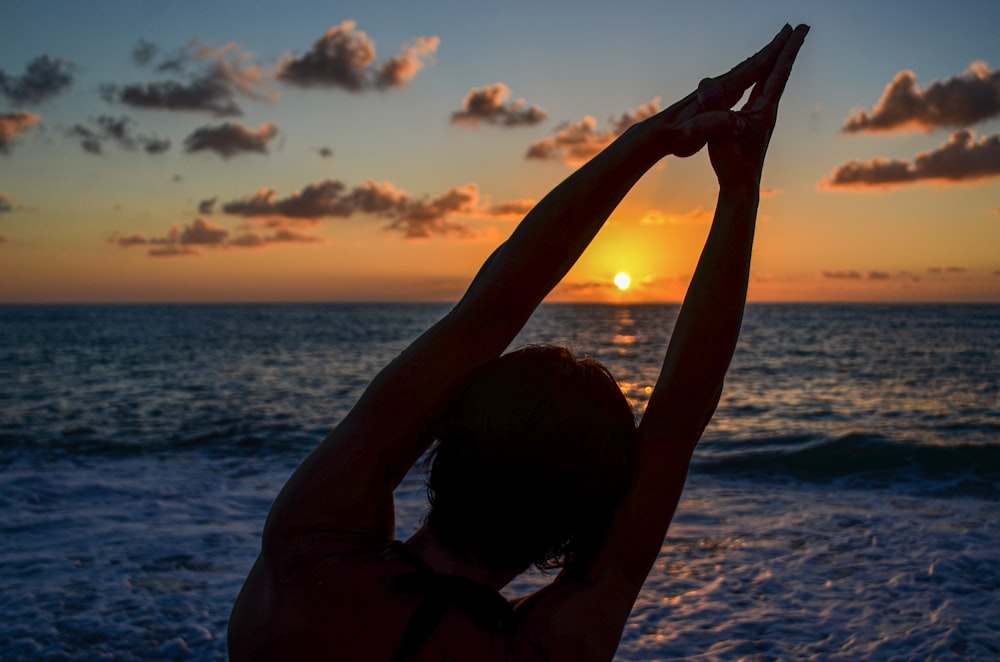 silhueta da mulher que levanta as mãos na praia durante o pôr do sol