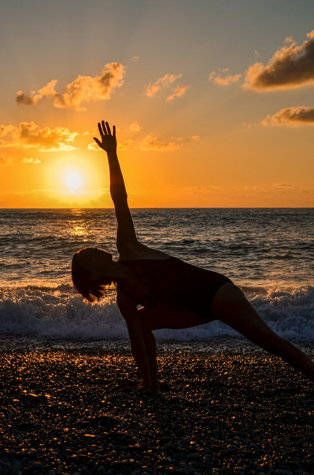 mulher em regata preta e shorts pretos fazendo yoga na praia durante o pôr do sol