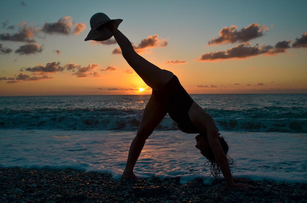 woman in black tank top and black shorts wearing white sun hat standing on rocky shore