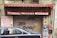 A closed storefront with the sign L'Ingenieur above, offering books, gifts, and toys. The metal shutter is covered in graffiti, and there is a prominent maroon-colored awning. A parked car half-blocks the view in front, with additional signs on the side listing office supplies, drawing materials, and photocopy services.