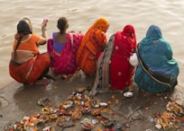 people in red and blue robe sitting on gray rock near body of water during daytime