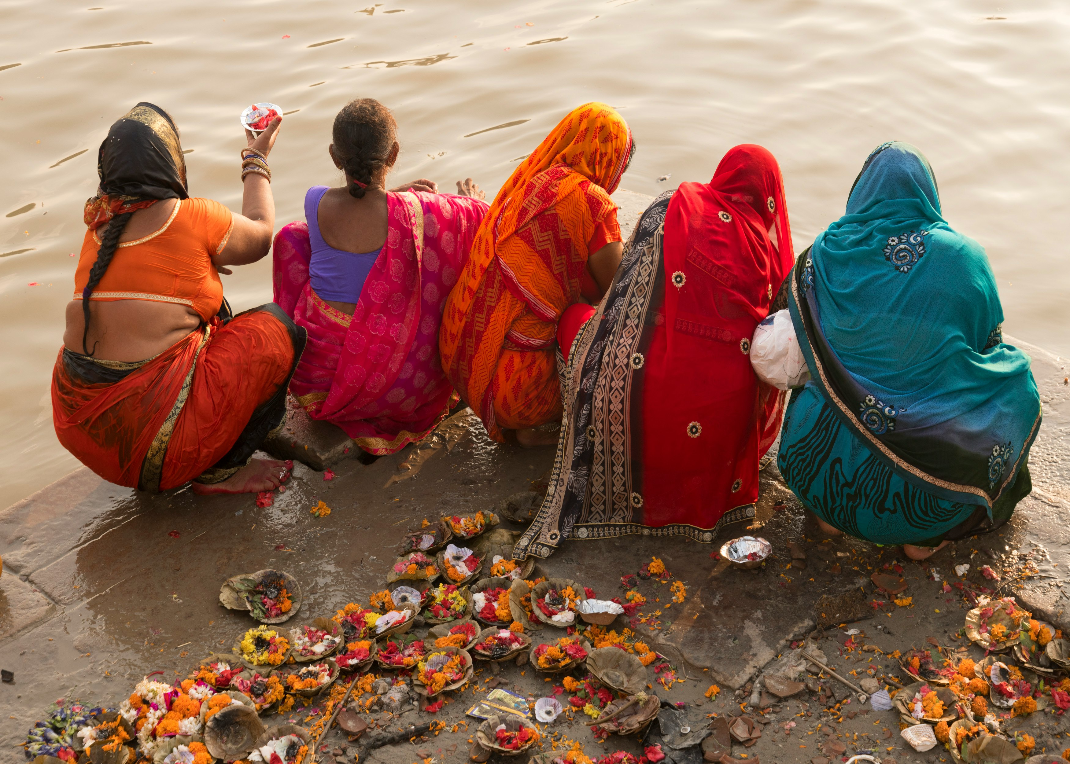 people in red and blue robe sitting on gray rock near body of water during daytime