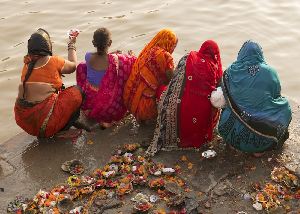 people in red and blue robe sitting on gray rock near body of water during daytime