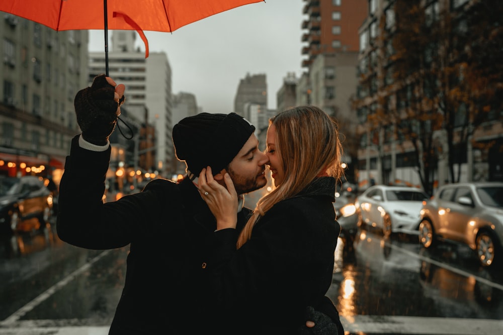 mulher na jaqueta preta que segura o guarda-chuva vermelho durante o dia