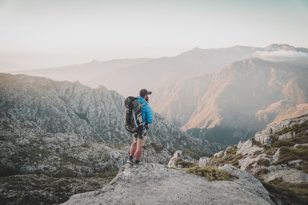 man in blue t-shirt and black shorts with hiking backpack walking on rocky mountain during