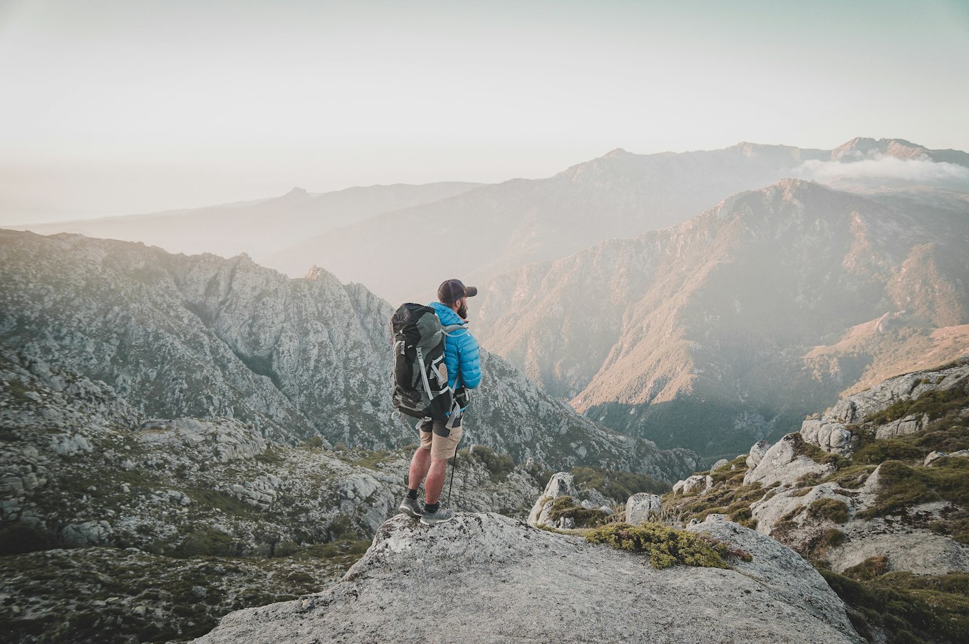 Man hiking with a backpack on a dramatic mountain summit, representing vitality and active health goals
