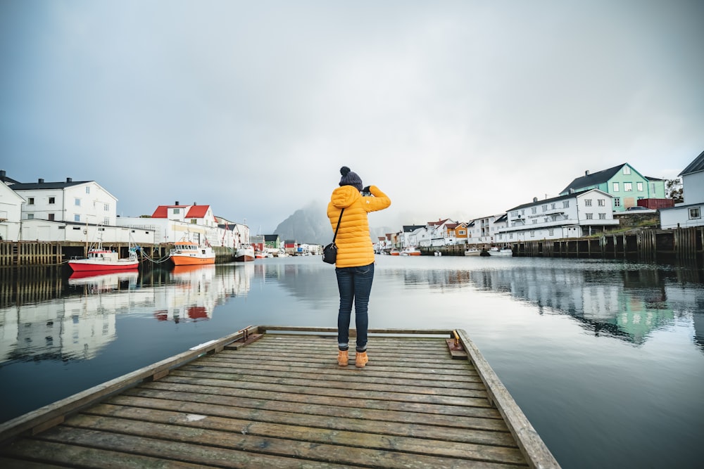 man in black jacket and blue denim jeans standing on wooden dock during daytime