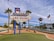 A famous sign welcomes visitors with the text 'Welcome to Fabulous Las Vegas, Nevada' in bright colors. Surrounded by palm trees, the scene features a clear blue sky with scattered clouds. In the background, iconic Las Vegas architecture and an American flag are visible, contributing to a lively and iconic city landscape.