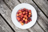 A vibrant orange stoneware plate set on a rustic wooden table with fresh fruit.