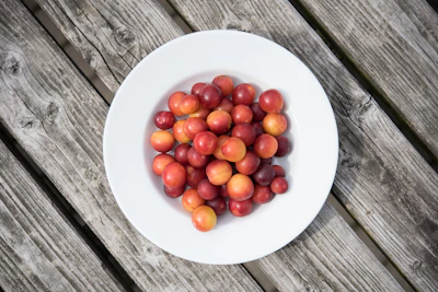 A vibrant orange stoneware plate set on a rustic wooden table with fresh fruit.