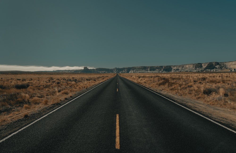 black asphalt road between brown grass field under blue sky during daytime