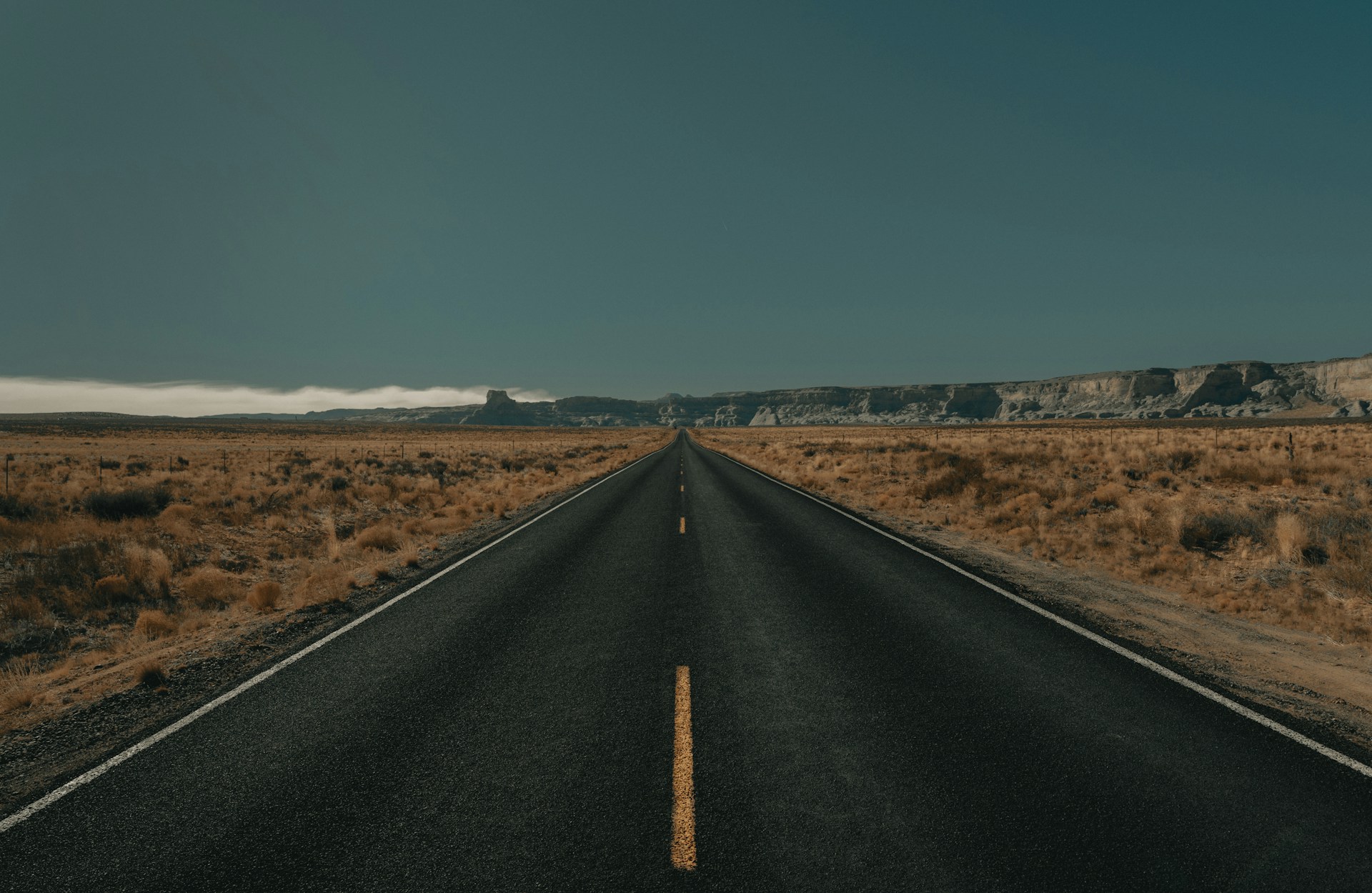 black asphalt road between brown grass field under blue sky during daytime