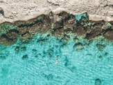 person in blue water near brown rock formation during daytime