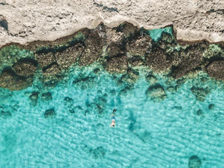 person in blue water near brown rock formation during daytime