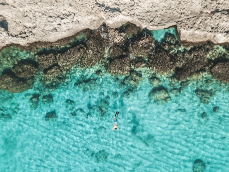 person in blue water near brown rock formation during daytime
