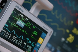 A medical monitor displays various vital signs and readings, including an ECG line showing heart activity, numbers indicating SPO2 levels, and blood pressure. The screen is prominently labeled with 'DEMO', and the monitor is manufactured by Mindray.