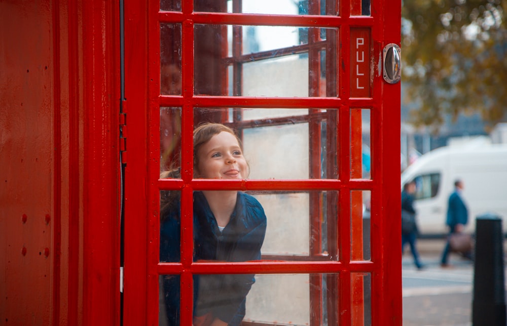 Donna in camicia nera a maniche lunghe appoggiata alla cabina telefonica rossa