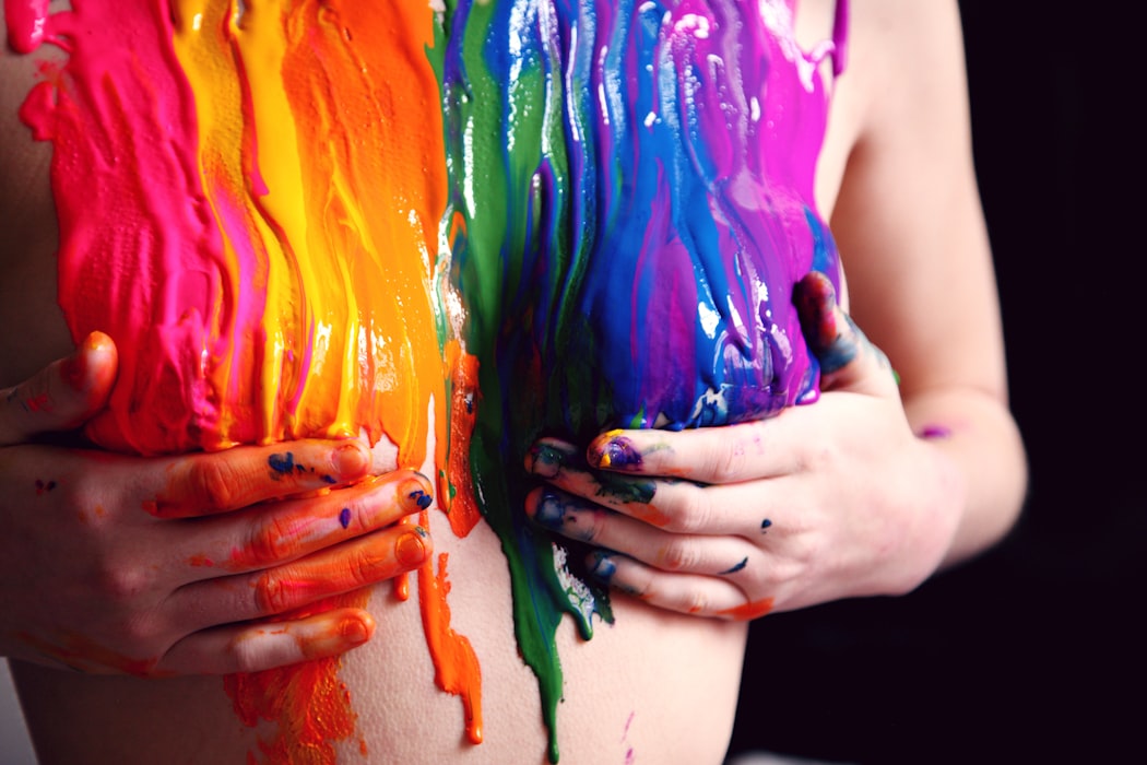 Naked female read upper part of body with liquid colors running down the skin, covering the breast, with two hands holding the boobs
