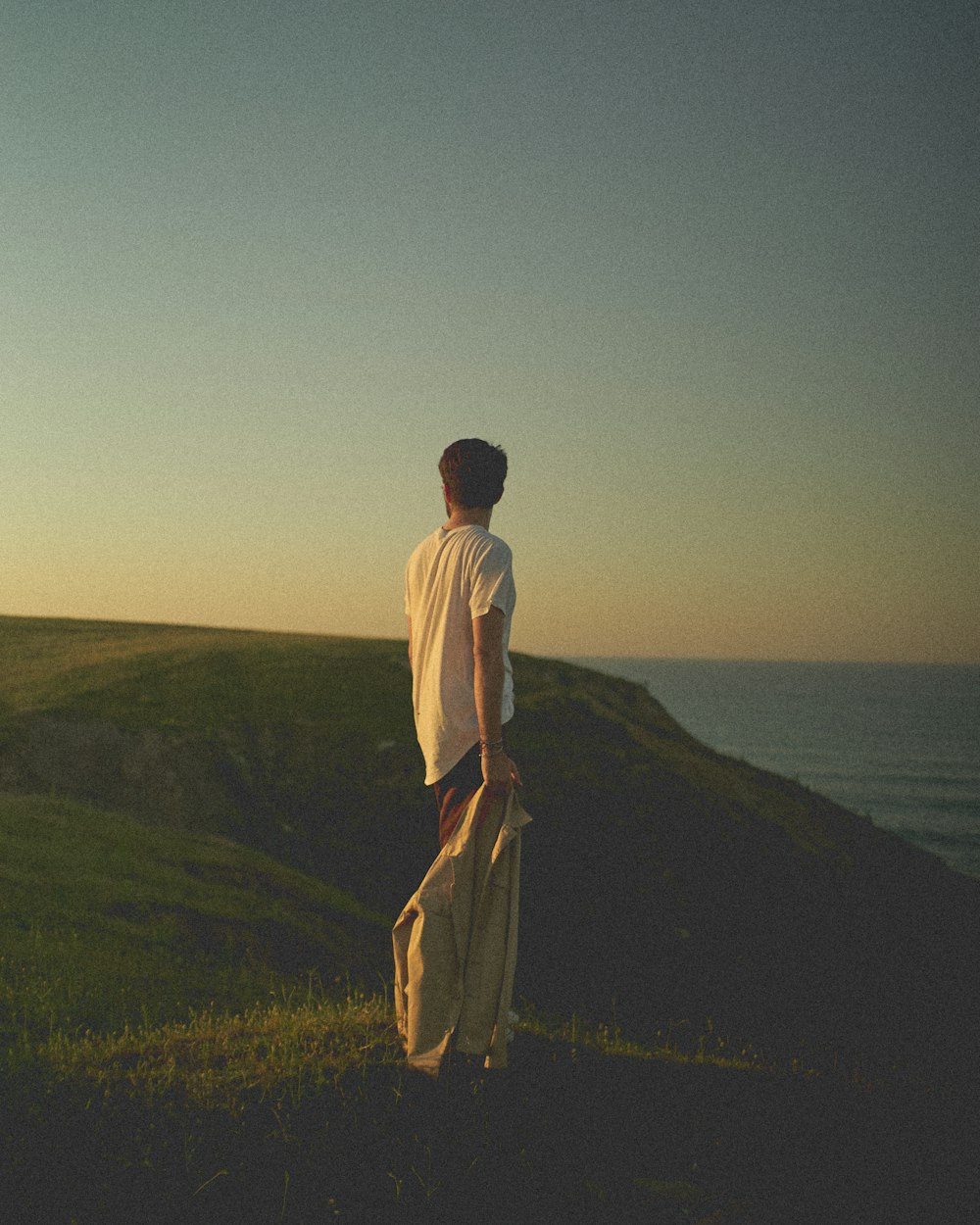 man in white shirt and brown pants standing on green grass field near body of water